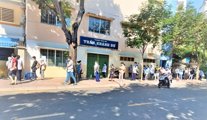 Các thí sinh được lực lượng công an và dân phòng hướng dẫn giữ khoảng cách an toàn trước điểm thi Trường Tiểu học Trần Khánh Dư (quận 1 - TP. HCM).