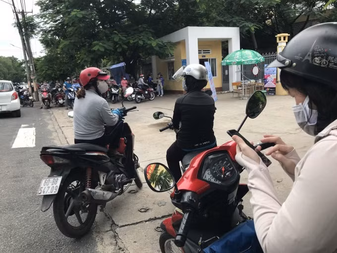 Phụ huynh thực hiện giãn cách, lướt điện thoại trong lúc chờ đón thí sinh.