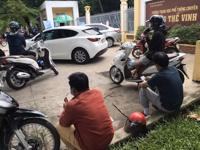 Các phụ huynh ngồi giữ khoảng cách trước một điểm thi ở TP. Biên Hòa.