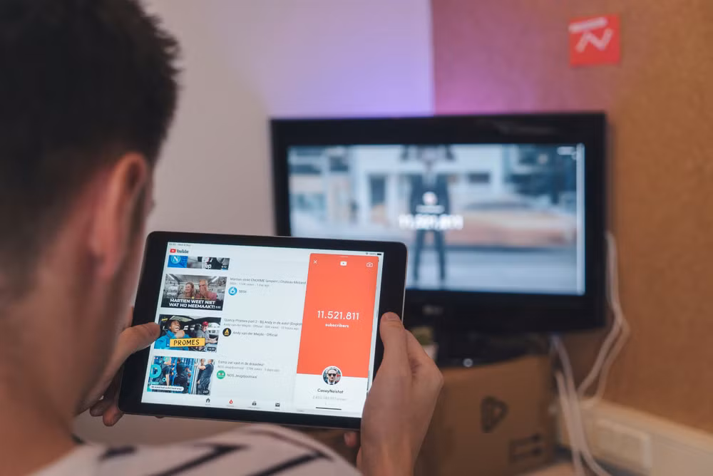 người đàn ông đang lướt máy tính bảng khi ngồi trước TV
