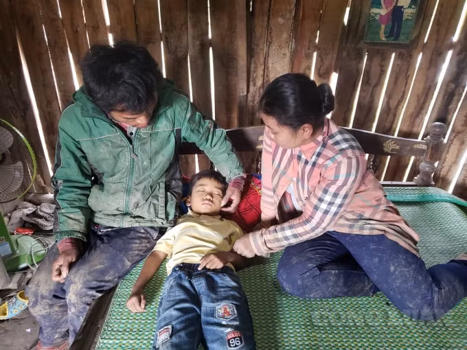 Vợ chồng anh Biêng và chị Xun bận bộ áo quần còn dính bùn đất ngồi nhìn con lên cơn đau mà lòng quặn thắt. Ảnh: Cái Văn Long.