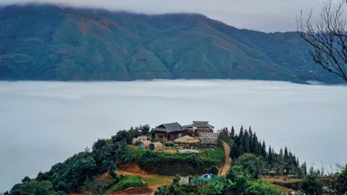 Một ngôi nhà nằm trên ngọn núi, xung quanh là 1 làn mây trắng.