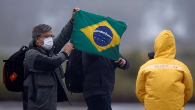 2 người Brazil trở về từ Vũ Hán cầm trên tay quốc kỳ hôm 9/2. Ảnh: Reuters