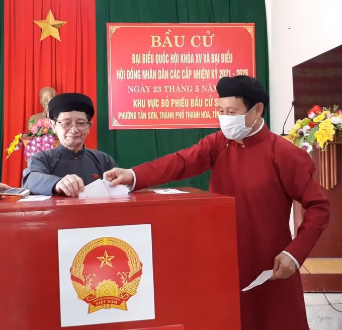 Anh Lê Việt Dũng (phải), cán bộ Ban Dân tộc tỉnh Thanh Hóa mặc áo dài ngũ thân đi bầu cử tại phường Tân Sơn, TP. Thanh Hóa. Theo anh Dũng, đây là cách để anh thể hiện tình yêu đối với các giá trị văn hóa truyền thống. Ảnh: FBNV