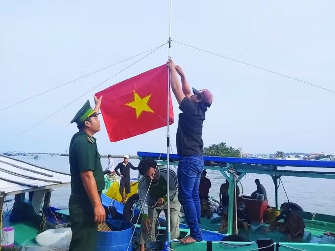 Cán bộ Đồn Biên phòng Cửa khẩu Cảng Dương Đông, huyện Phú Quốc, tỉnh Kiên Giang giúp ngư dân treo cờ Tổ quốc lên tàu – Ảnh: Hoàng Tuấn.