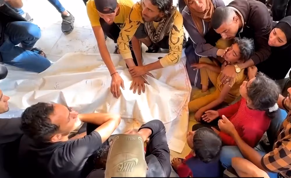 Người dân Gaza đau buồn bên cạnh thi thể một người thân bị thiệt mạng trong lúc nhận hàng cứu trợ của GHF. Ảnh chụp màn hình
