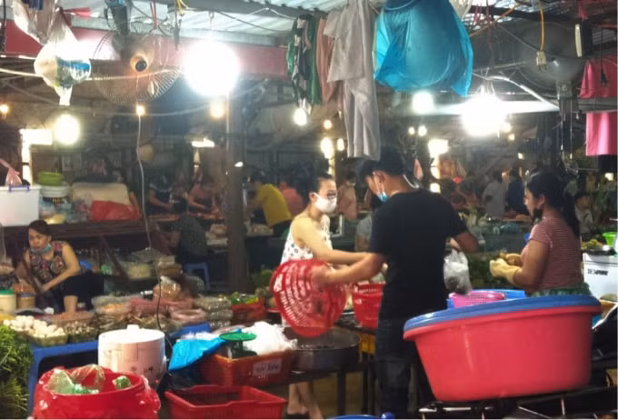 Tương tự tại chợ Nhân Chính (quận Thanh Xuân), người bán hàng đeo khẩu trang không đúng quy định đang giao tiếp với khách hàng.