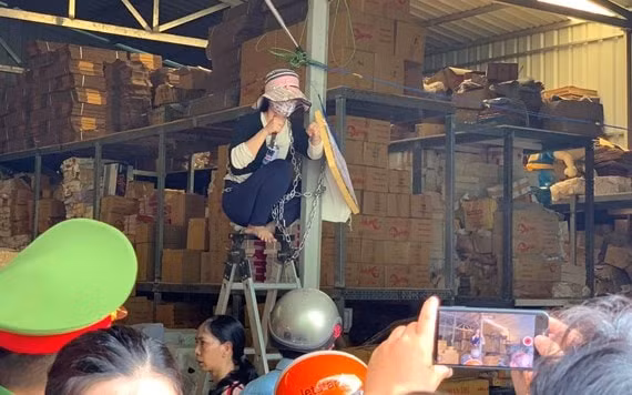 Một phụ nữ ngồi trên một chiếc thang cao, quấn dây xích trói mình vào một cây cột nhằm không cho lực lượng chức năng cưỡng chế.