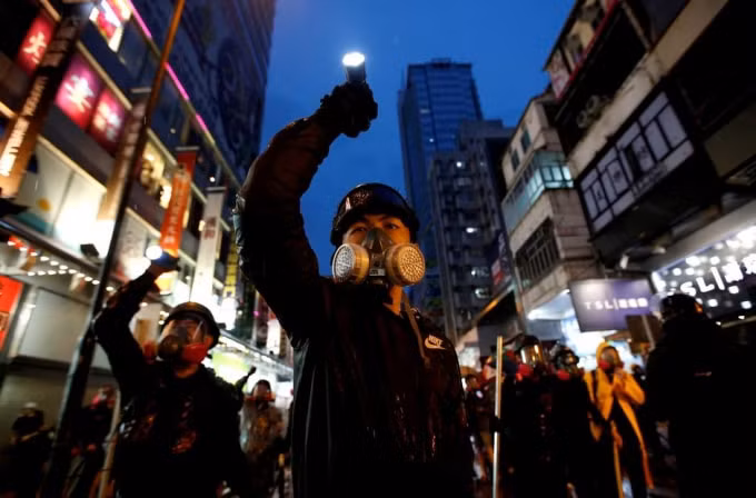 Một người biểu tinh đeo mặt nạ cầm đèn pin biểu tình ở Hong Kong. Ảnh: Reuters