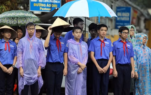 Học sinh trường THCS Hai Bà Trưng đội mưa chờ đoàn xe chở linh cữu nguyên Chủ tịch nước, Đại tướng Lê Đức Anh đi qua ngã tư Pasteur - Võ Thị Sáu, gần nhà riêng của ông. Ảnh: Thành Nguyễn.