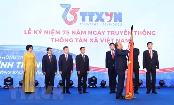 Thủ tướng Nguyễn Xuân Phúc gắn Huân chương Lao động hạng Nhất lên lá cờ truyền thống của Thông tấn xã Việt Nam. Ảnh: TTXVN