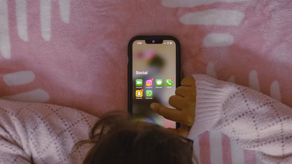 một người đang nằm trên giường và cầm điện thoại di động.