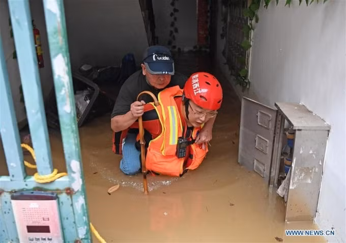 Nhân viên cứu hộ đang trợ giúp một ông lão đến nơi an toàn. Ảnh: Tân Hoa Xã.