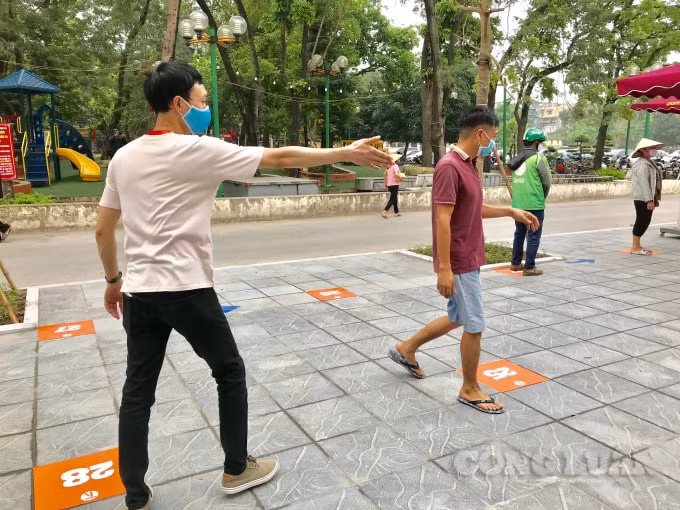 Các tình nguyện viên hướng dẫn người dân đứng đúng vị trí các ô để giữ khoảng khách an toàn khi chờ nhận nhận gạo