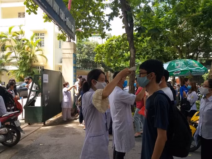 Các em được cán bộ y tế phụ trách điểm thi đo thân nhiệt một cách cẩn thận (ảnh Minh Triết).