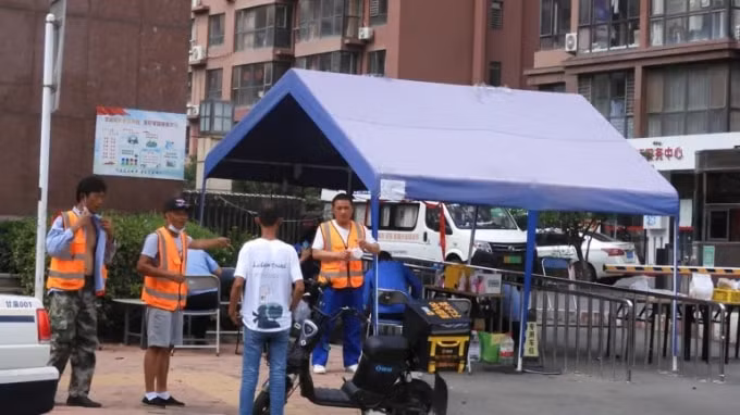 Cơ quan chức năng giám sát lối vào của một tòa nhà chung cư đã bị phong toả sau khi phát hiện thấy các ổ nhiễm trùng, ở Đại Liên vào ngày 4 tháng 8. Ảnh: Nikkei