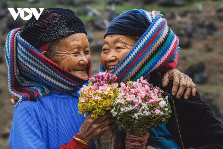 Cụ bà người Lô Lô trong trang phục truyền thống ngồi bên hiên nhà.