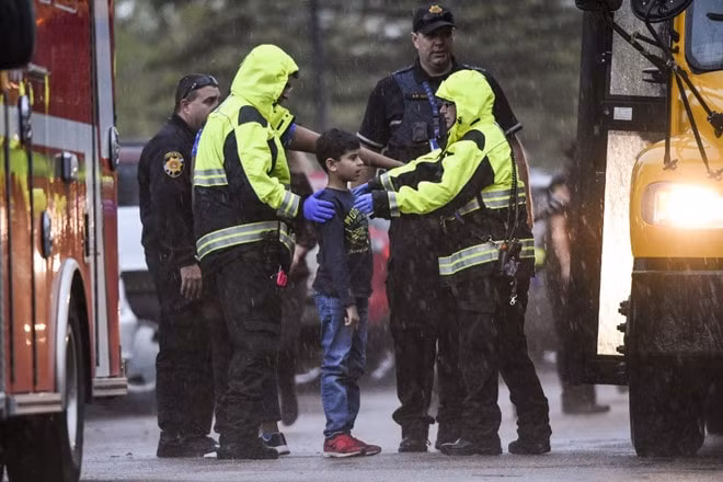 Một học sinh được đưa lên xe buýt để di chuyển khỏi hiện trường. Ảnh: AFP