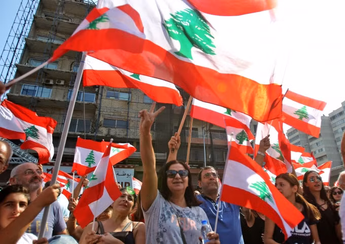 Người biểu tình Lebanon giương cao quốc kỳ trước một rào chắn tạm được dựng trên một con đường chính ở khu vực Jal el-Dib, phía bắc thủ đô Beirut vào ngày 21 tháng 10 năm 2019. Ảnh: Getty